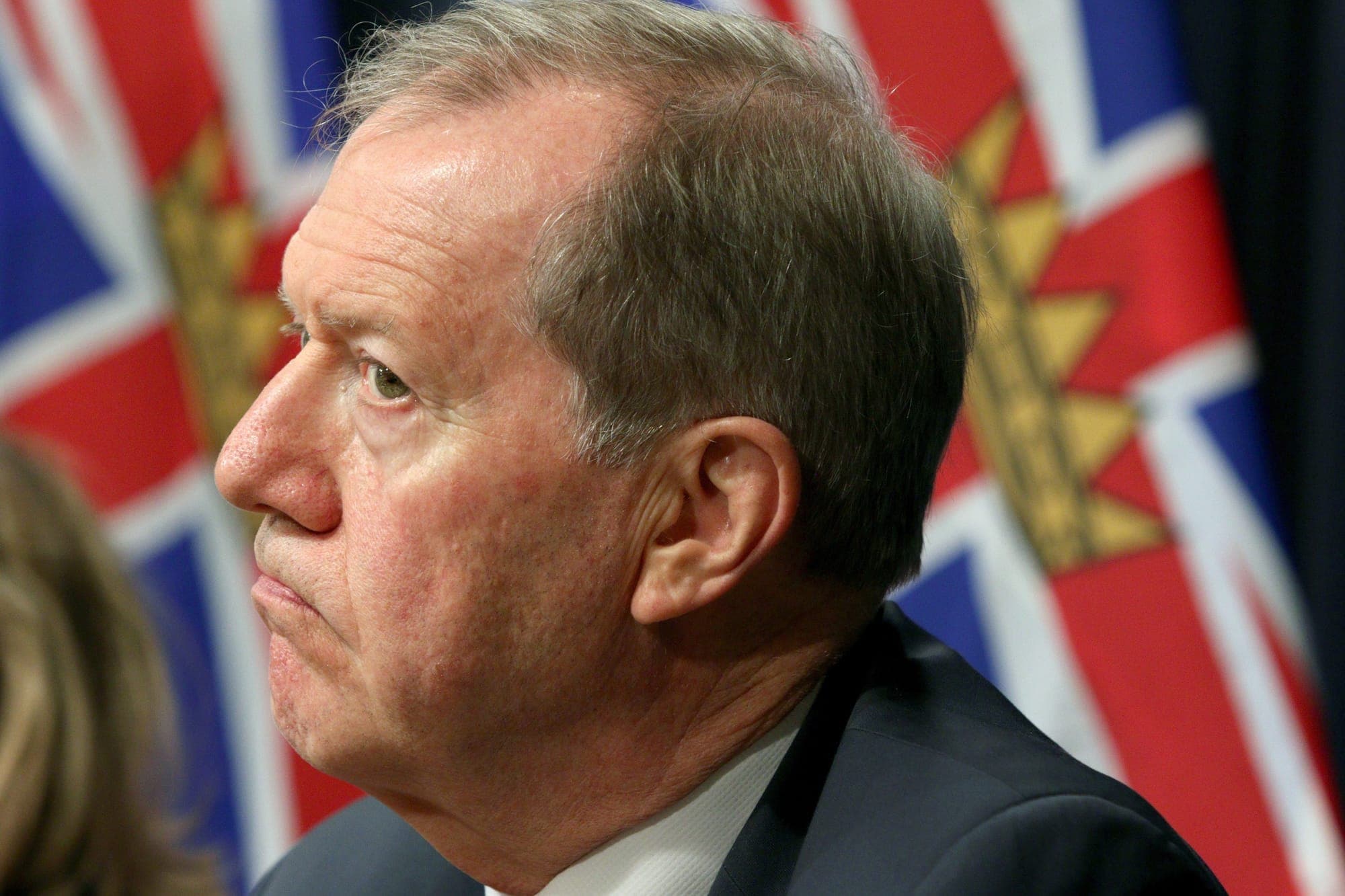 Side profile of a man in a suite with a British Columbian flag in the background.