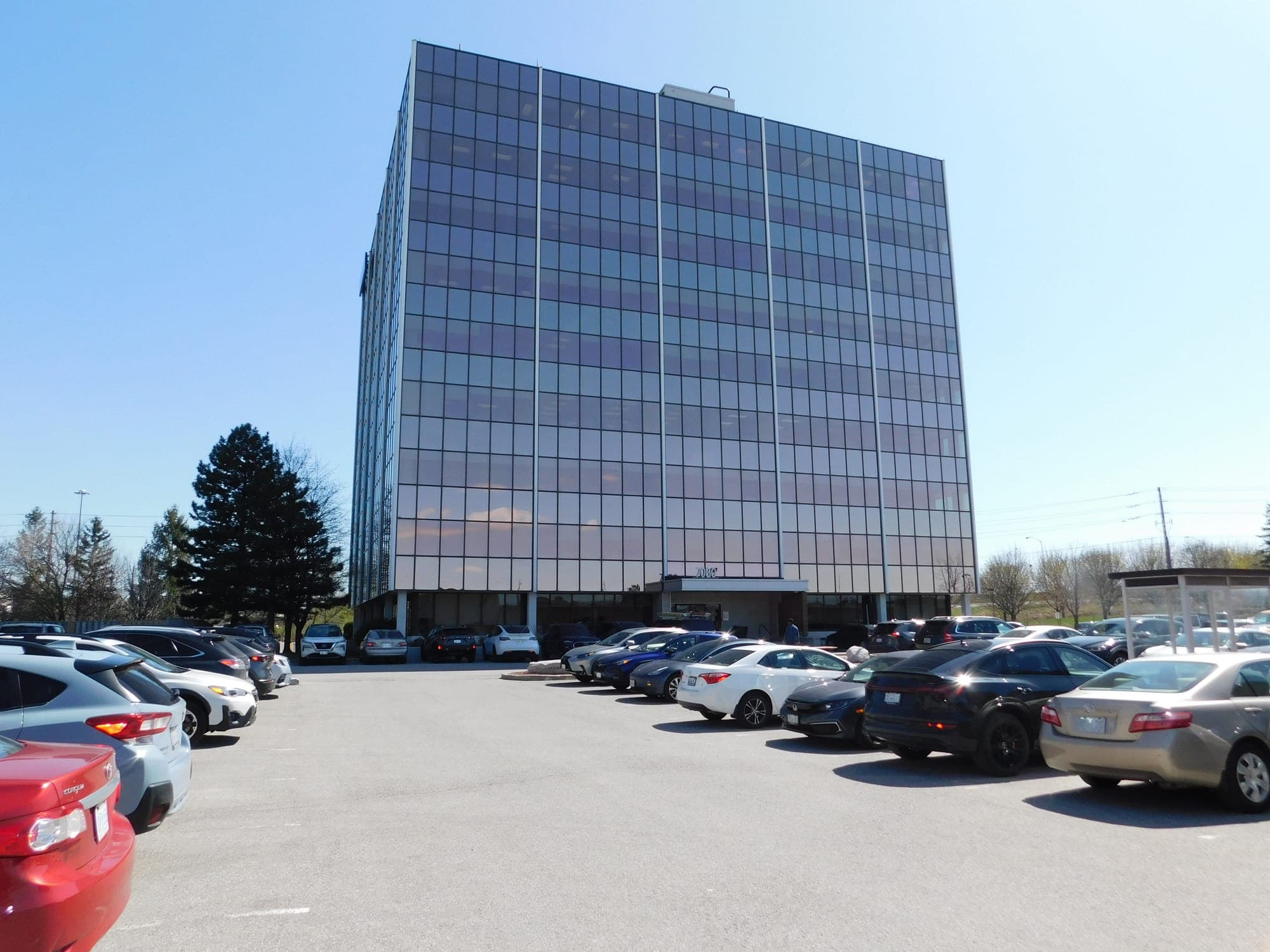 A tall, glass office building in front of a parking lot.