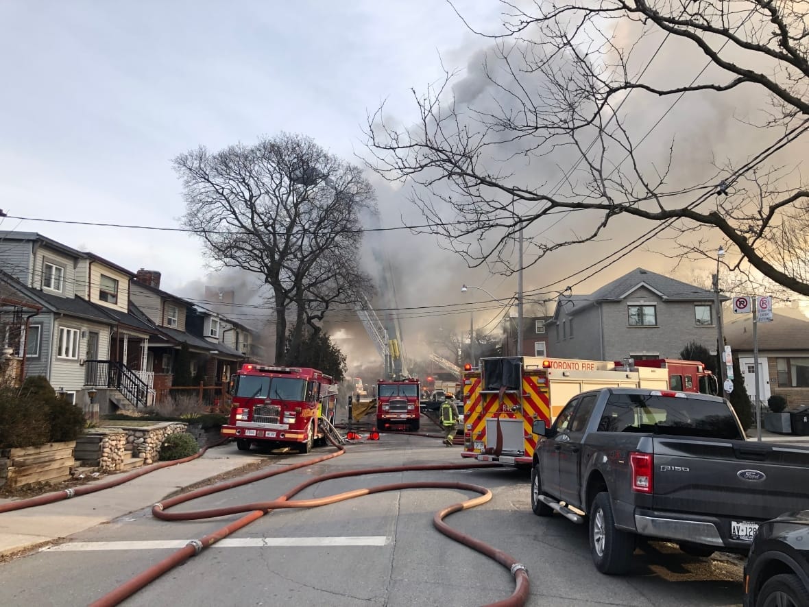 Three fire trucks are parked on a street as they fight a fire and the sky is full of smoke 