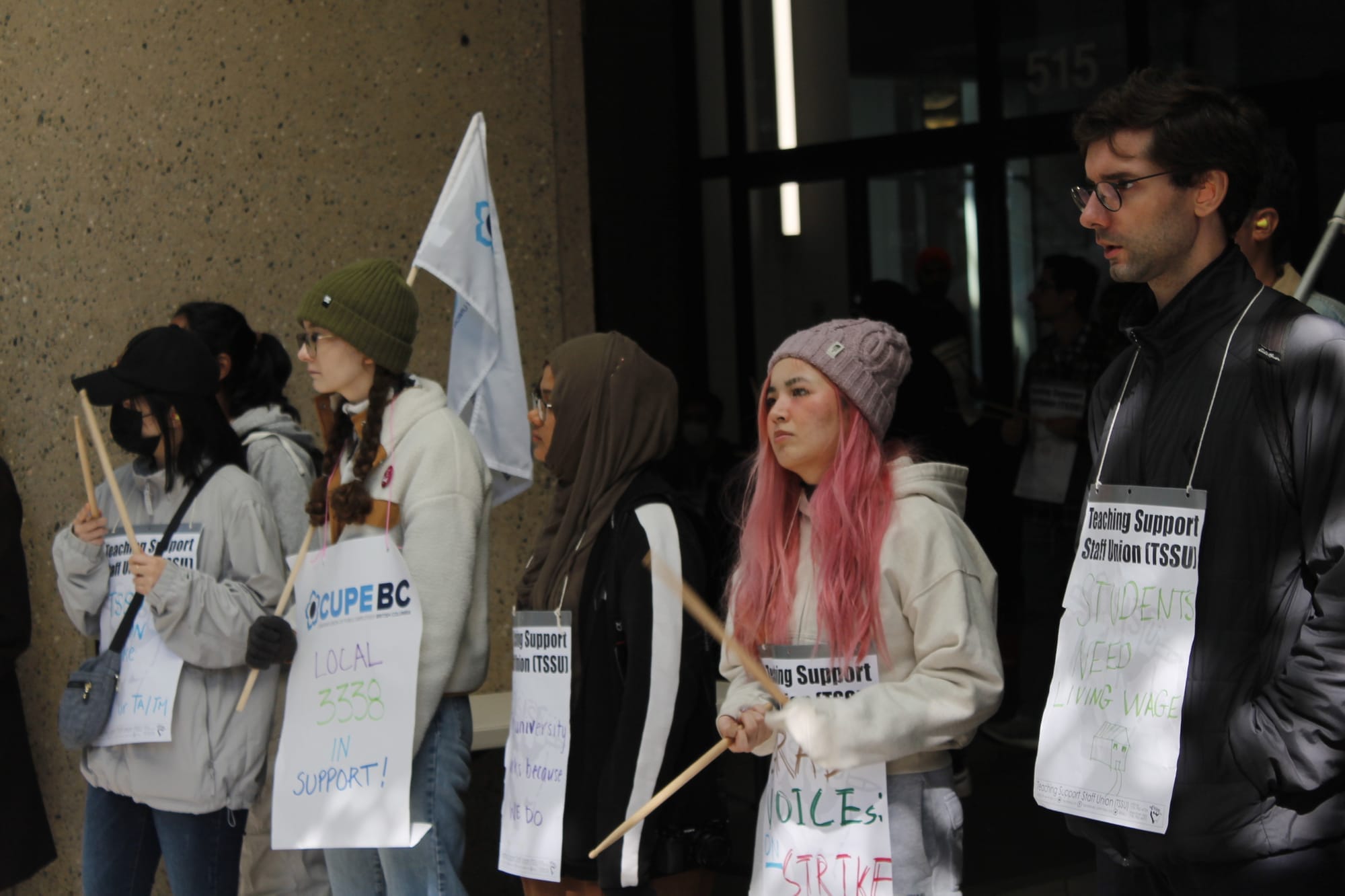 Striking workers wearing white signs stand outside Simon Fraser University in Vancouver. 