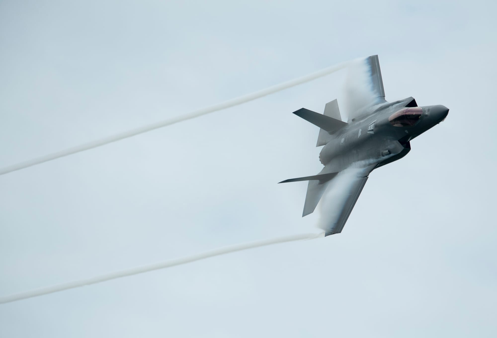 A silver fighter jet is pictured against a grey sky. 