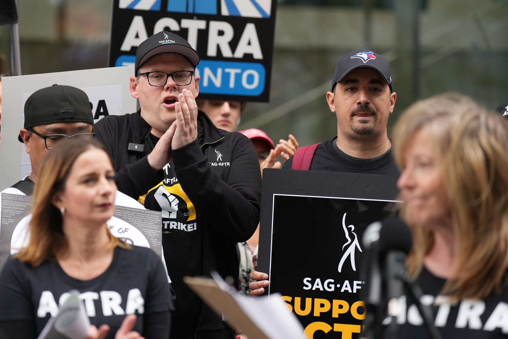 People are seen clapping and holding signs in support of ACTRA and SAG-AFTRA. 