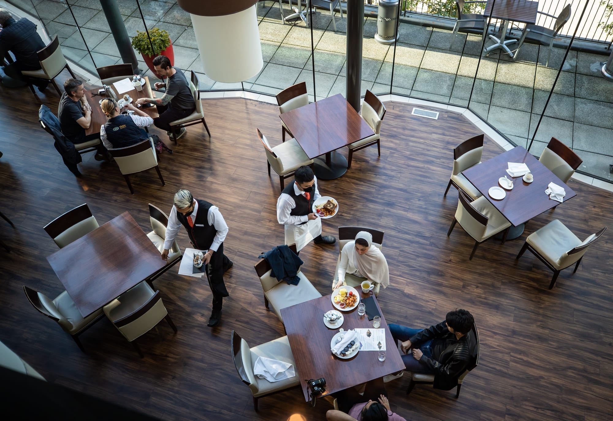 An overhead view of a server bringing a plate to a table of diners in a restaurant. 