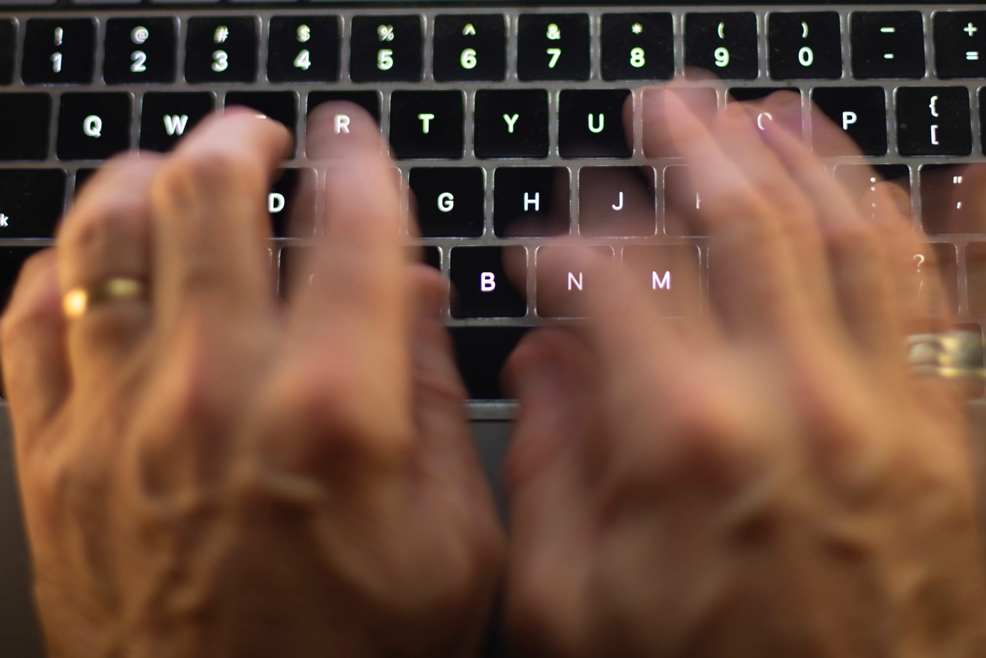 A blurry pair of hands typing on a black computer keyboard. 