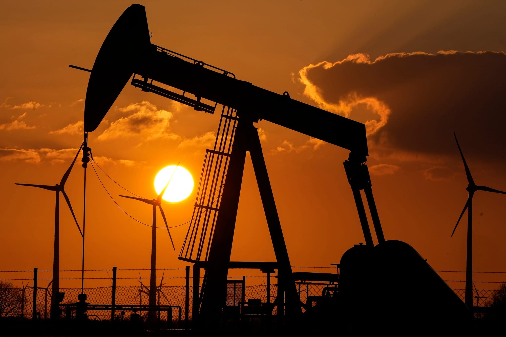 A pump jack is seen extracting oil at an oil field near wind turbines during sunset.