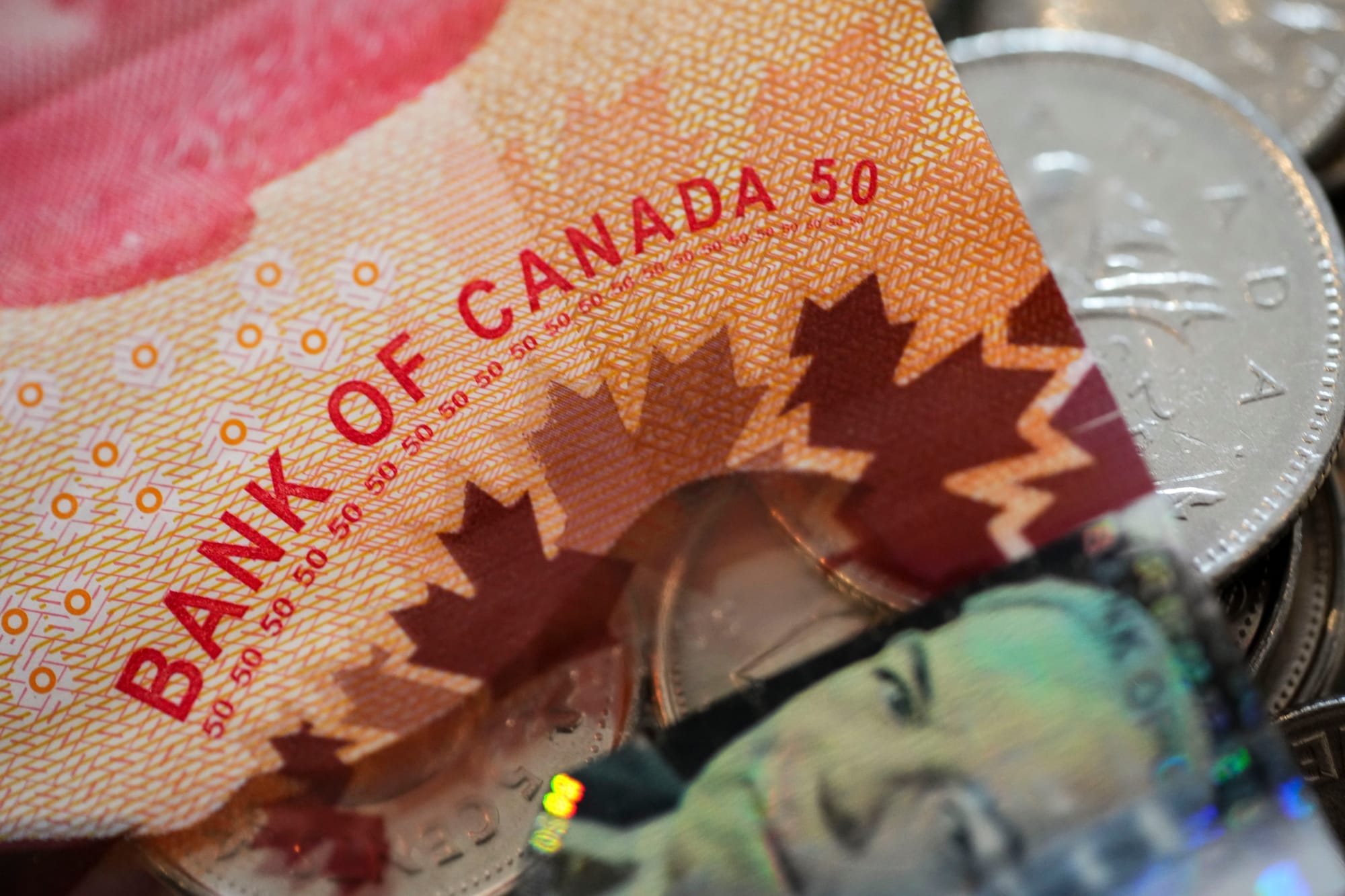 A $50 Canadian bill is shown in closeup, on top of a pile of coins.