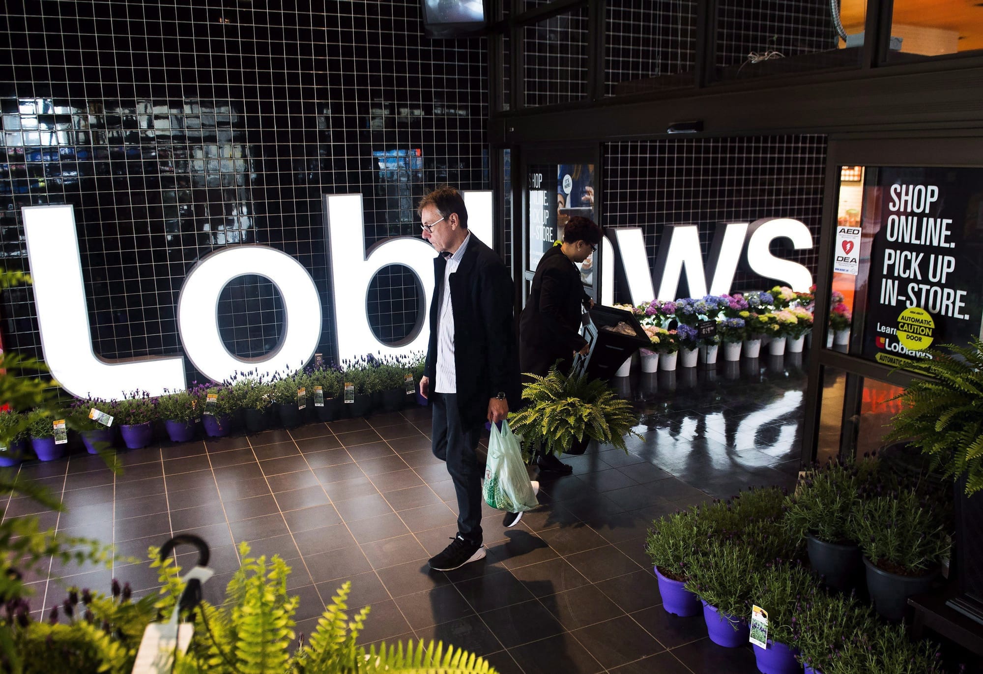 A person walks out of a grocery store illuminated by a light-up Loblaws sign in the background.