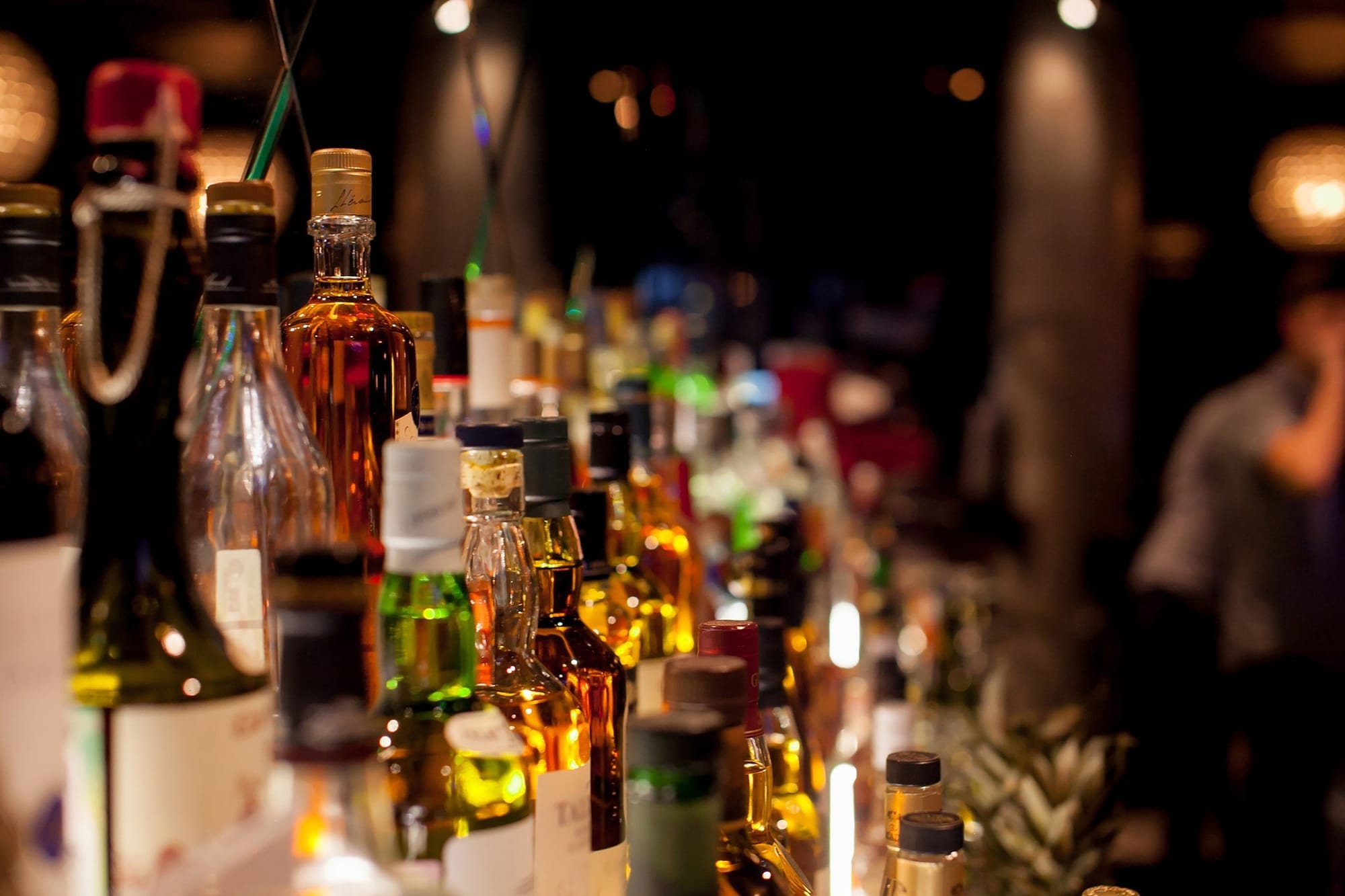 Bottles of spirits are lined up on shelves behind a bar