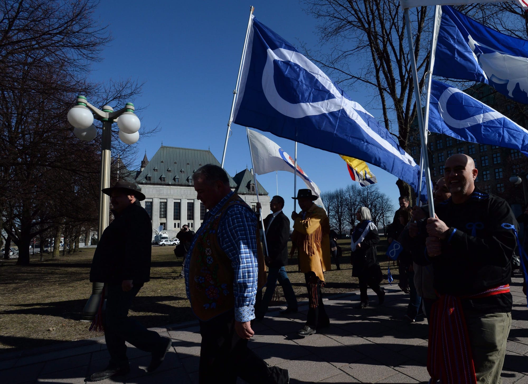 Several people march in front of a government building carrying Metis flags