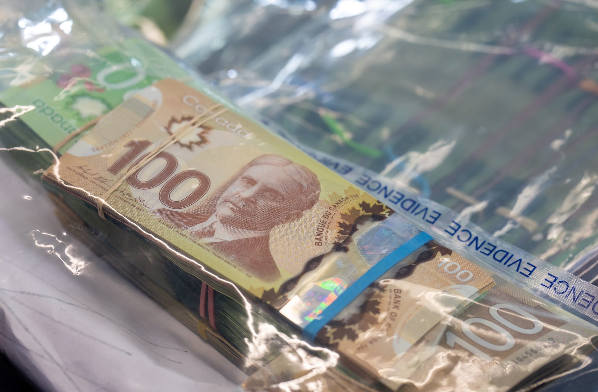 A stack of Canadian bills bound with an elastic band in a plastic bag labelled "evidence." 