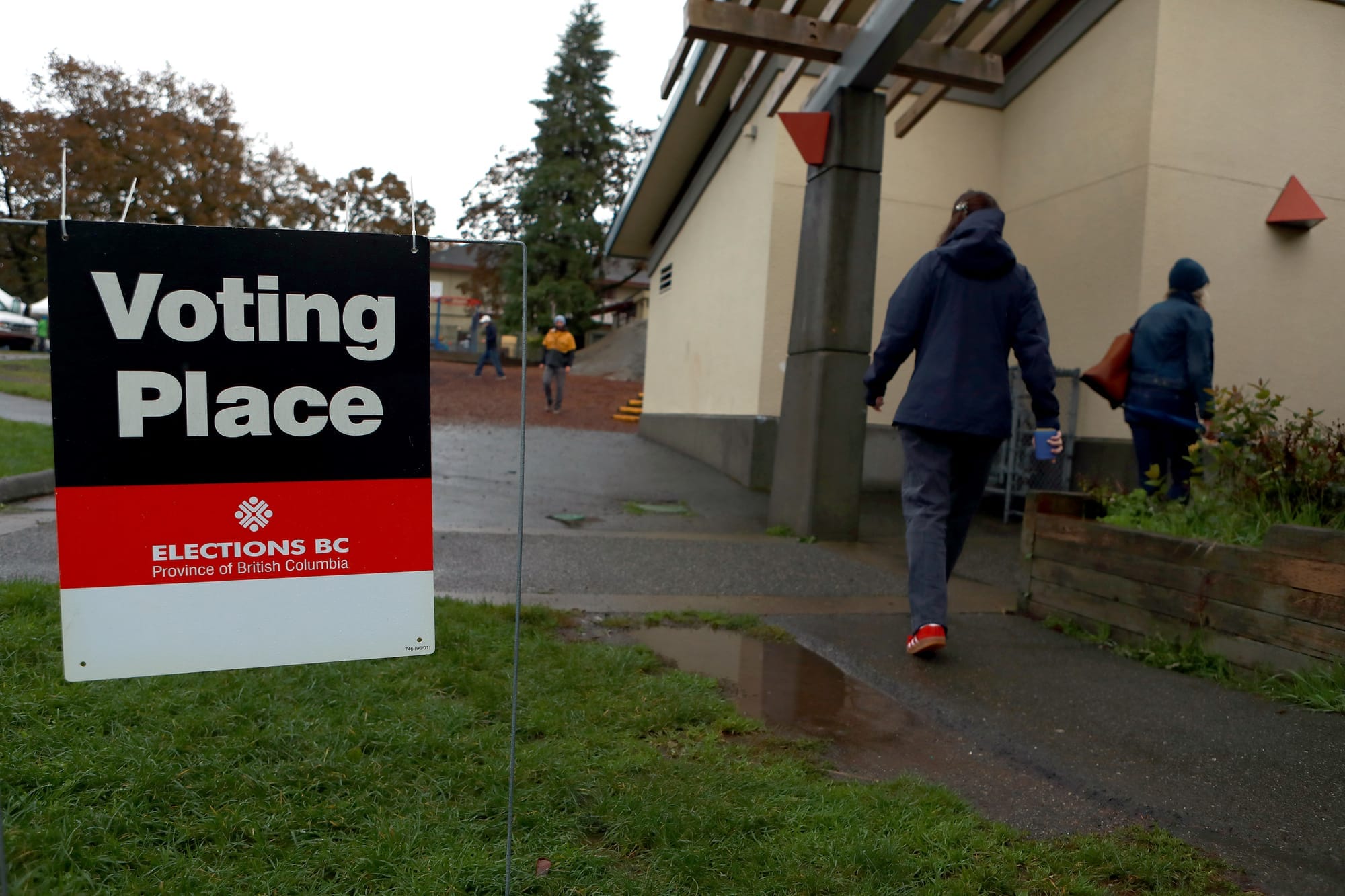 A black, red and white sign that says "Voting Place" is pictured next to two people walking into a low, white bulding.