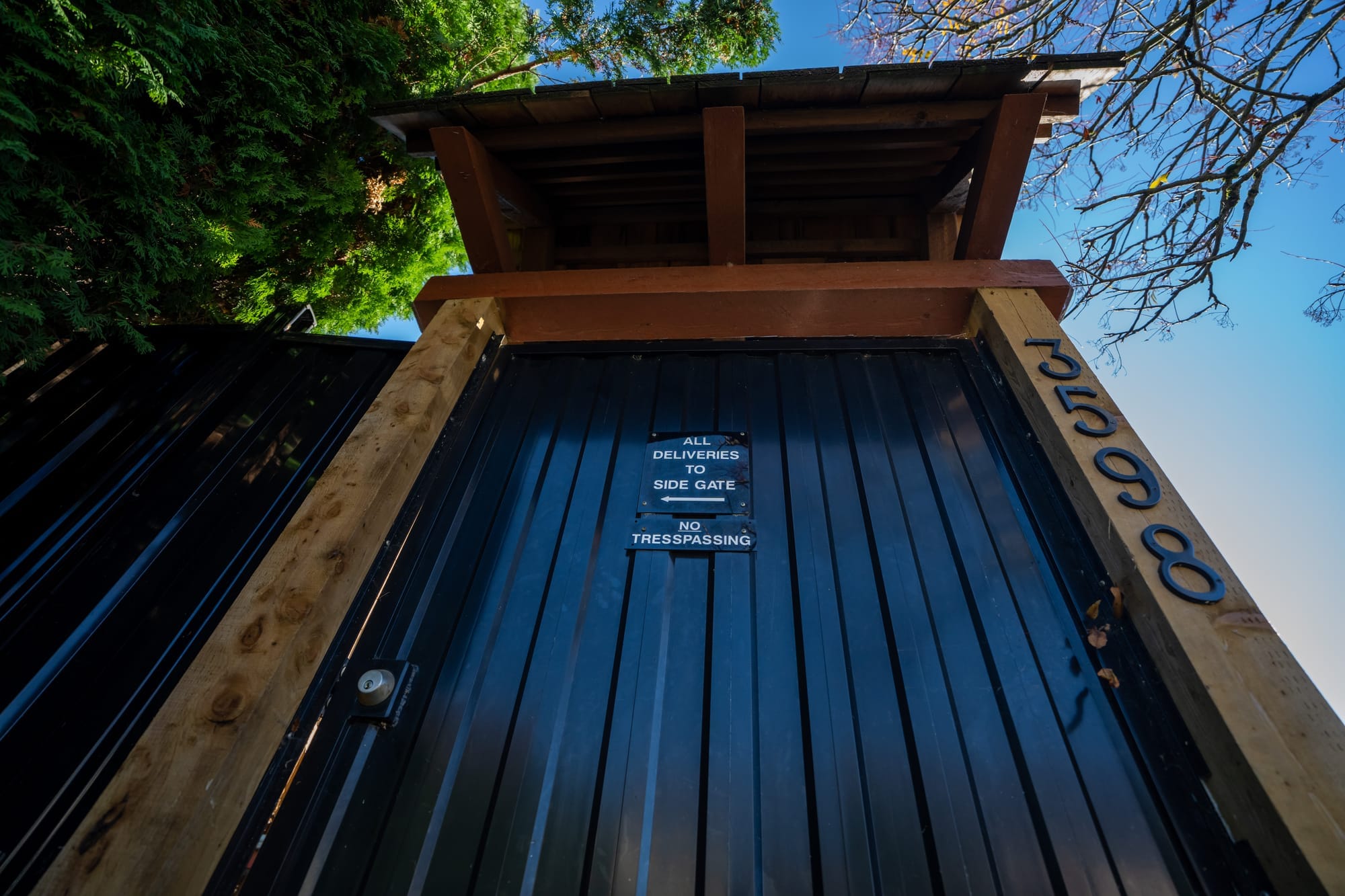 Upward perspective on a tall, wooden gate with a black metal door. 