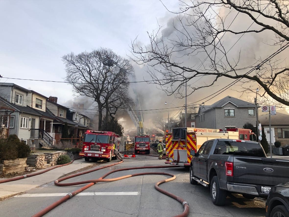 Three fire trucks are parked on a street as they fight a fire and the sky is full of smoke