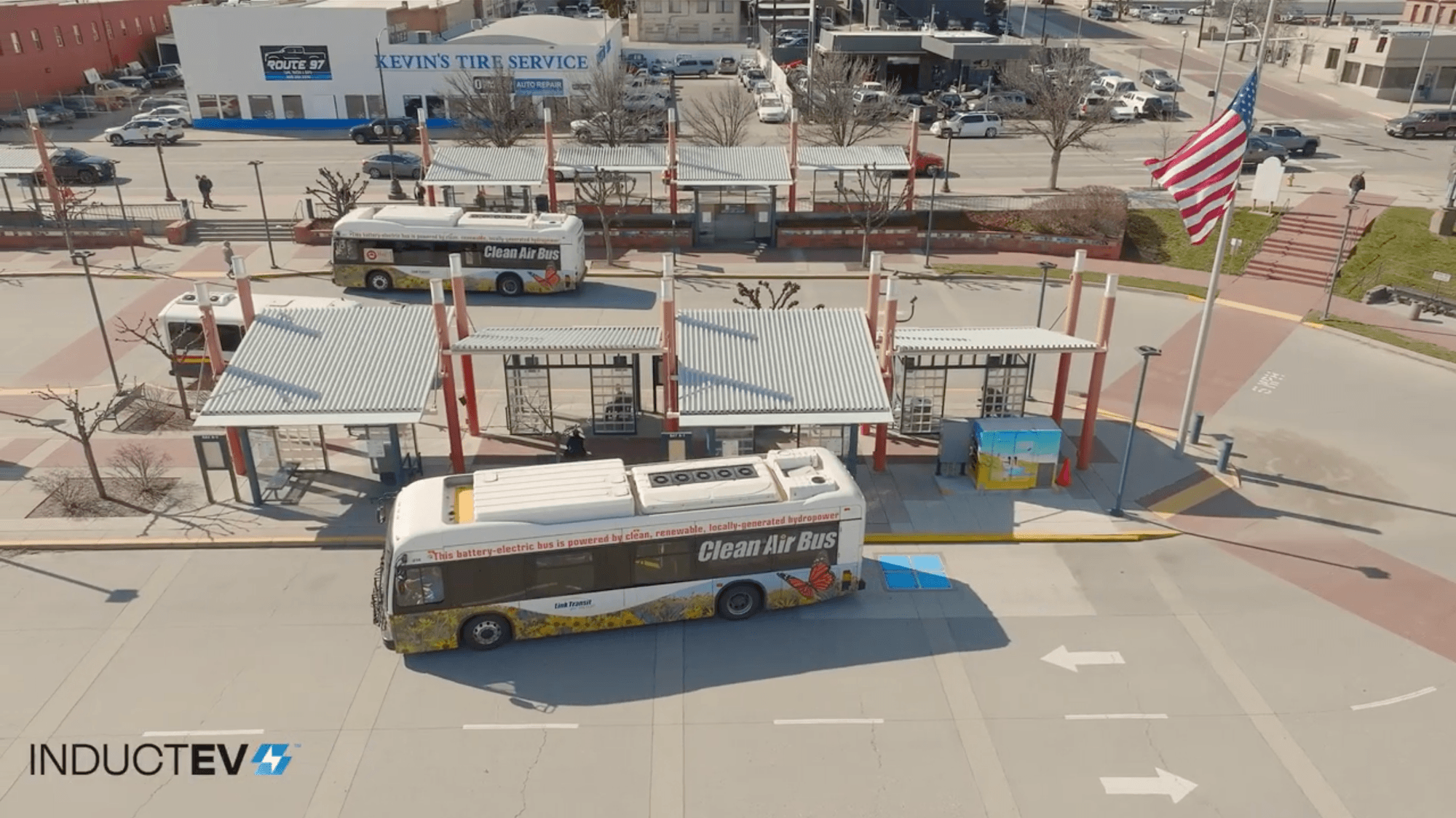Aerial shot of an electric bus driving away from an in-ground charging pad at a bus station.
