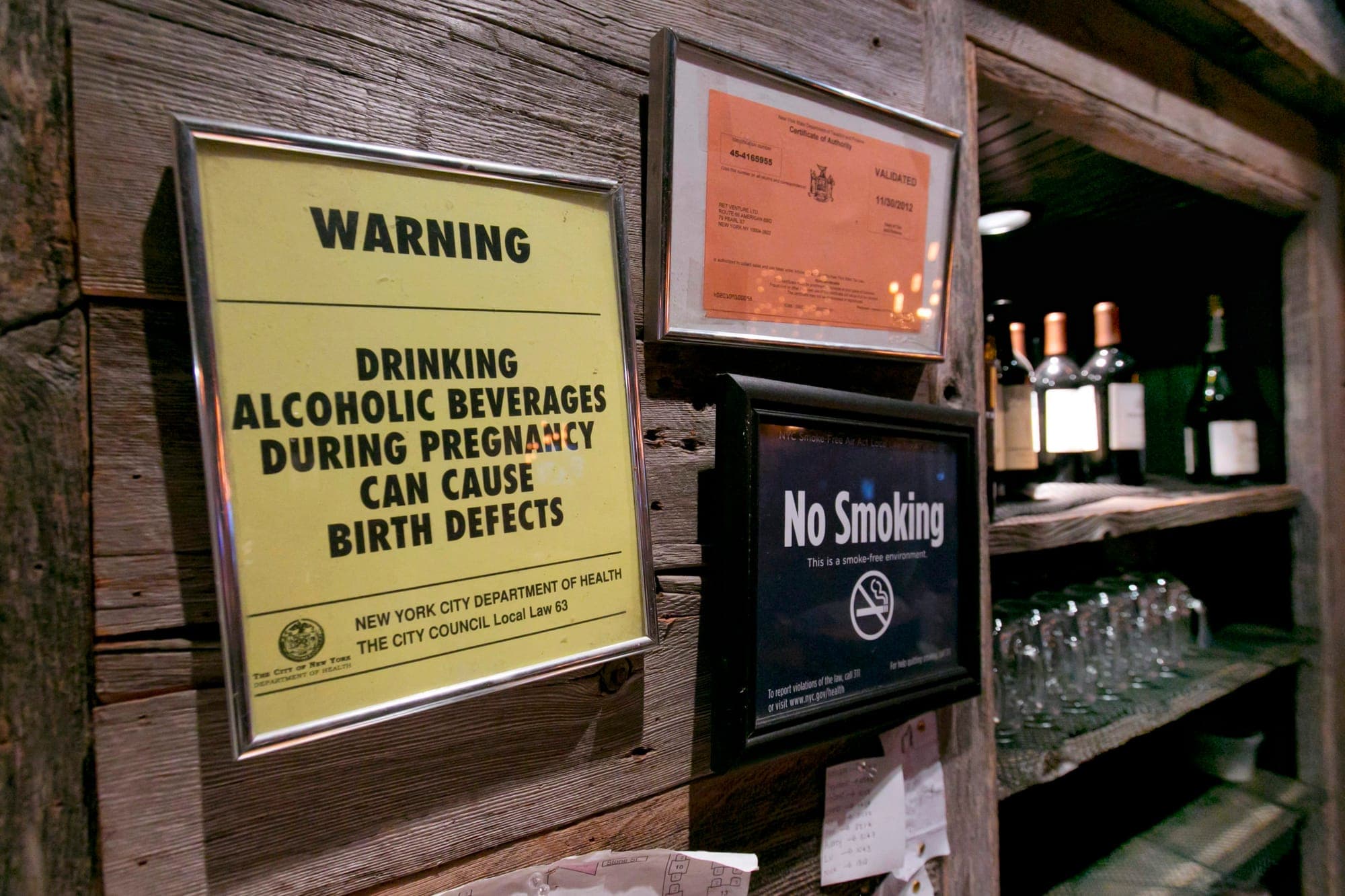 A sign behind a bar says "WARNING: DRINKING ALCOHOLIC BEVERAGES DURING PREGNANCY CAN CAUSE BIRTH DEFECTS"