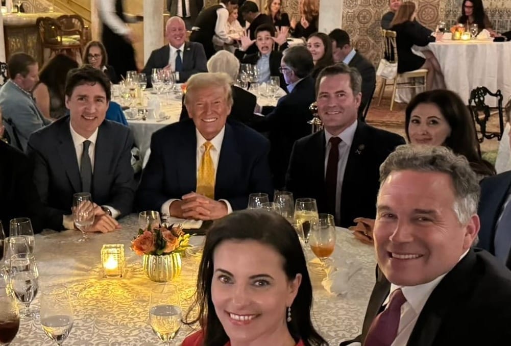 Guests dressed in formal attire and seated at a table in Mar-a-Lago's dining room look towards the camera and smile.