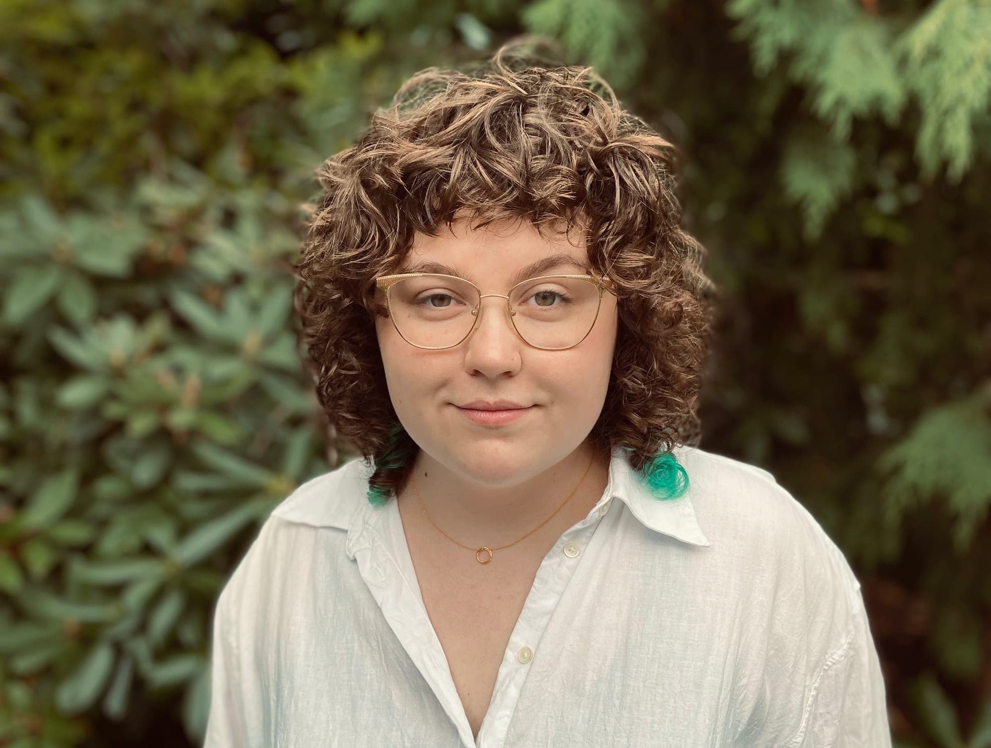 Sydney Dawson has curly brown hair and wears gold-framed glasses and a white collared shirt.