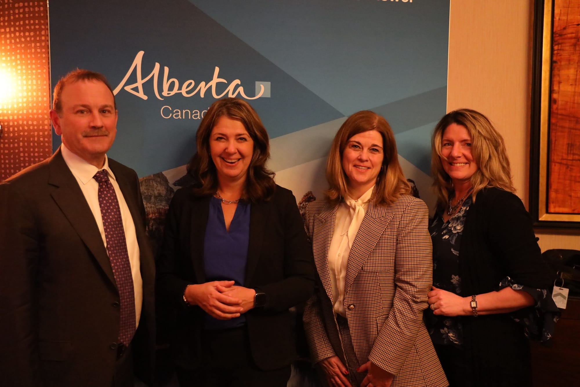 Four people in suit jackets smile for a photo together in front of a sign that says Alberta, Canada.