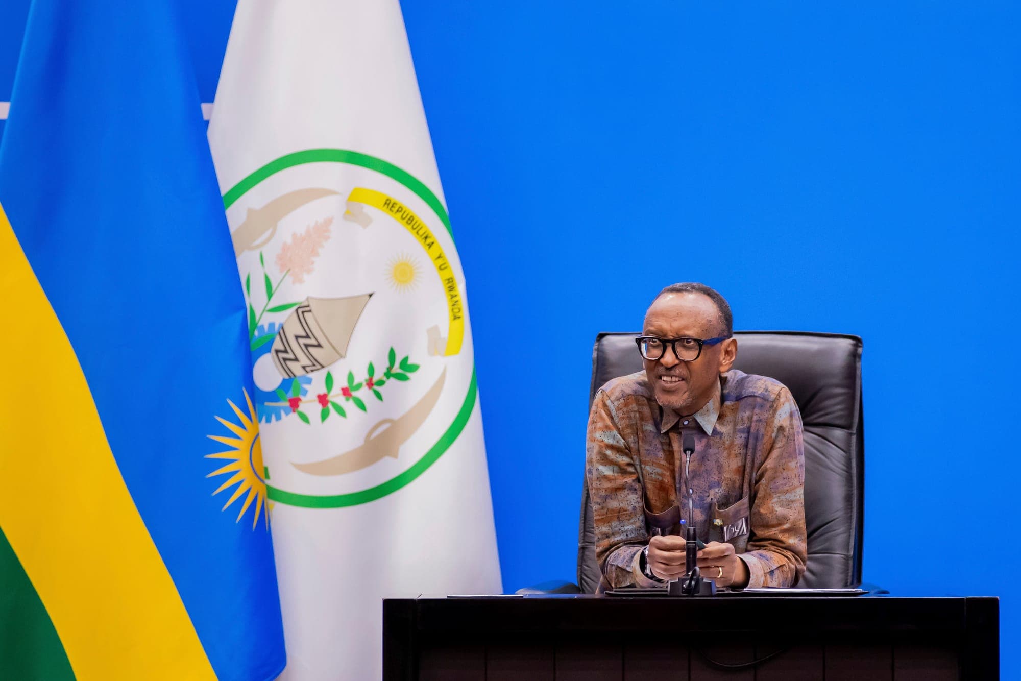 President Paul Kagame is seated at a microphone in front of a Rwandan flag
