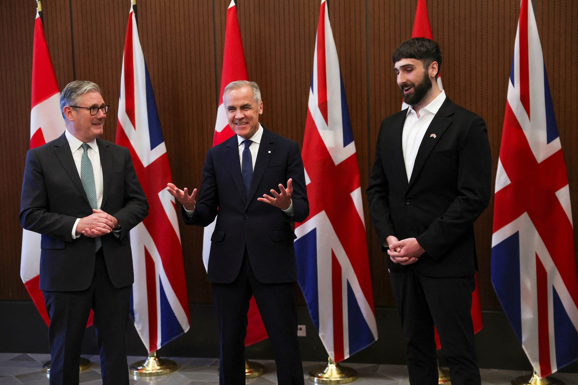 Keir Starmer, Mark Carney and Aidan Gomez wear suits in front of U.K. and Canadian flags