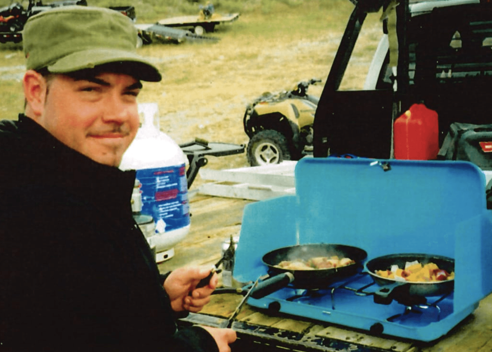 Mazin Zaim looks over his shoulder at the camera as he prepares food on a camping stove.