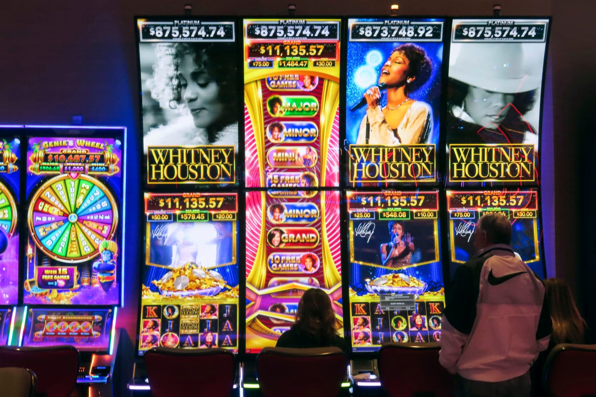 Gamblers sit at a row of Whitney Houston-themed slot machines in a casino.
