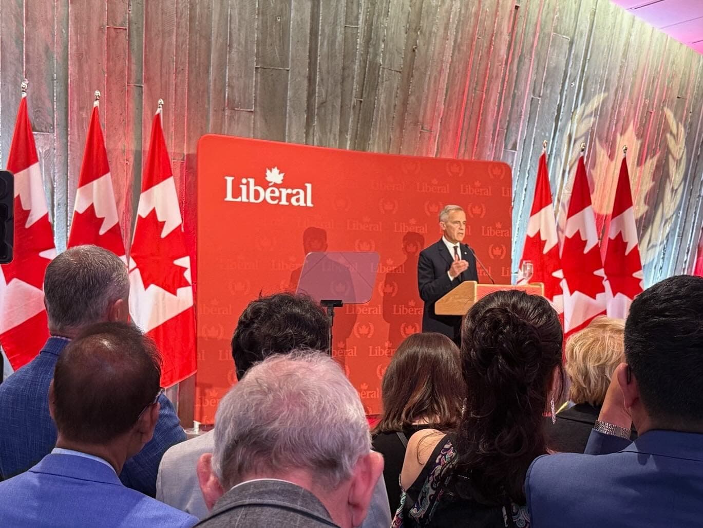 Prime Ministe Mark Carney speaks to a crowd with Canada flags and a Liberal Party sign behind him.