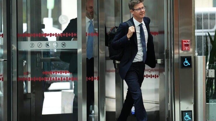 Galen Weston, dressed in a suit, exits a set of glass doors.