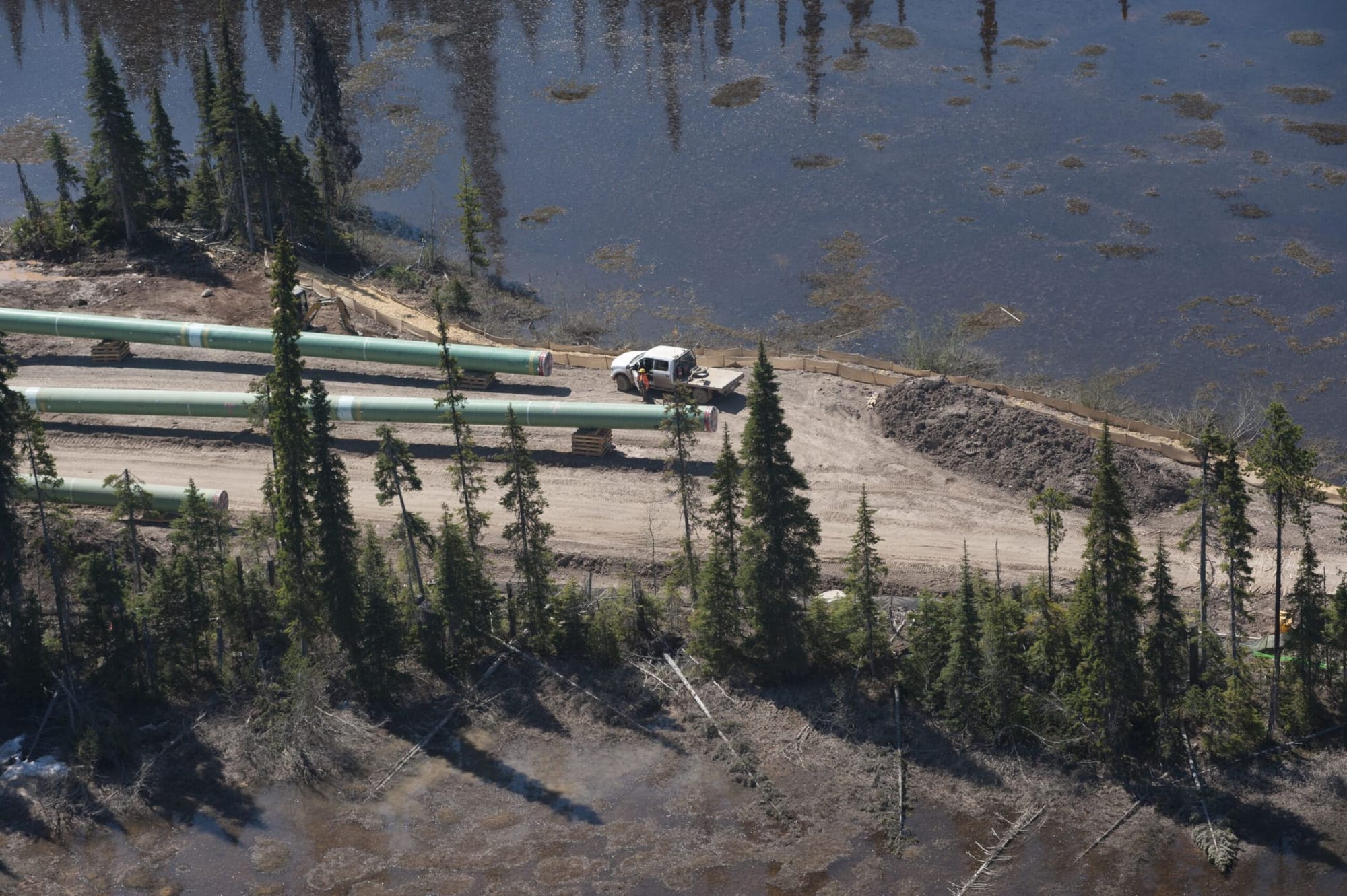 A white pick-up truck is pictured next to a lake. The truck is next to two pipelines under construction.