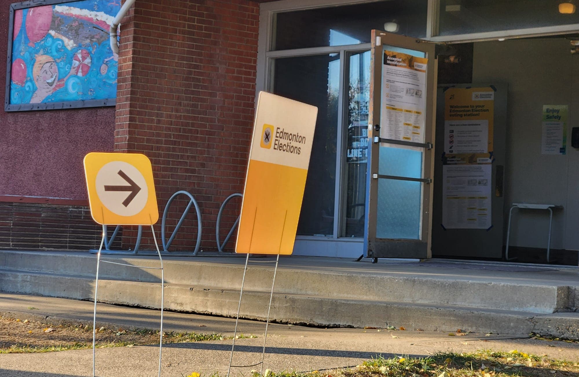 Two Edmonton Elections signs in front of a community league building direct voters to a polling station.