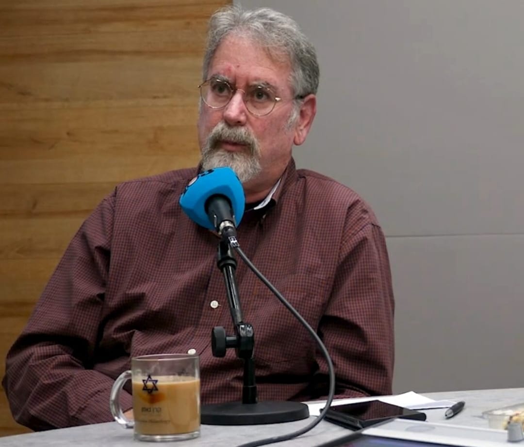 Chaim Katz, an older man with grey hair, bread and glasses, speaks into a microphone.
