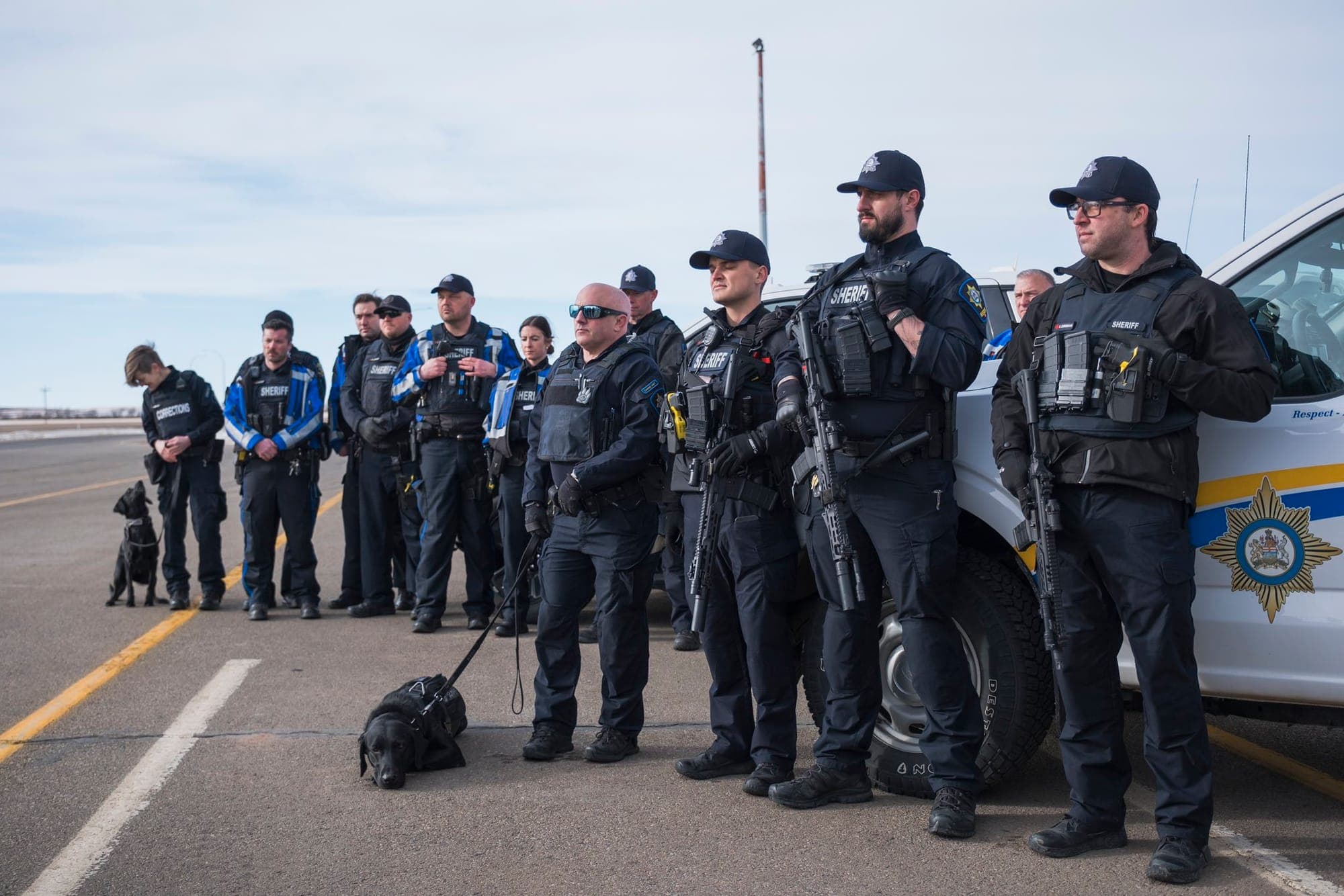 Uniformed police pose standing in a line on the side of a highway.