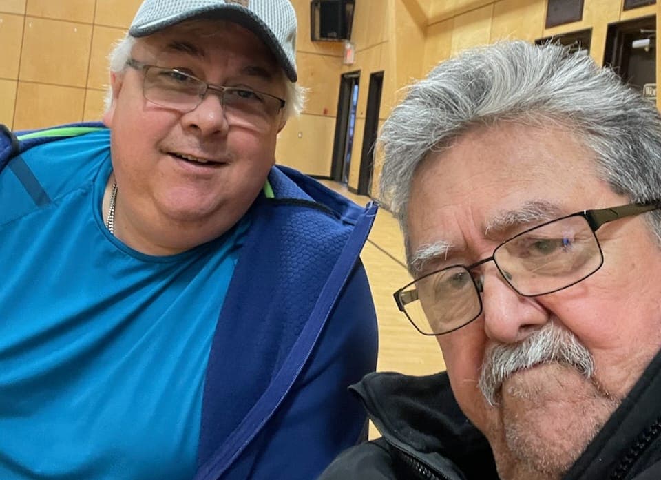 Terry Chase and Dorman Joseph, two grey haired men in glasses, pose together in a gymnasium.