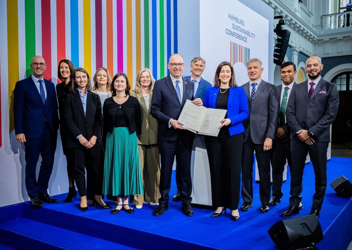 Twelve people pose for a photo. The people in the centr hold a signed document.