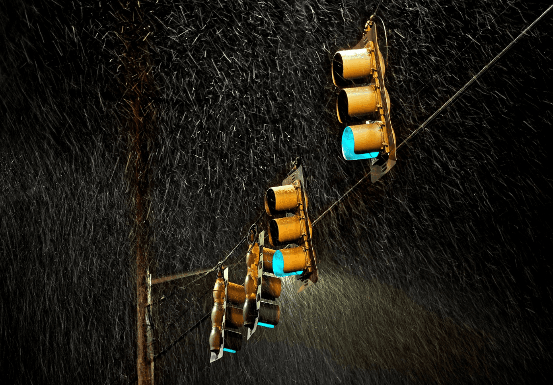 Traffic lights illuminated green are shown on a rainy night.