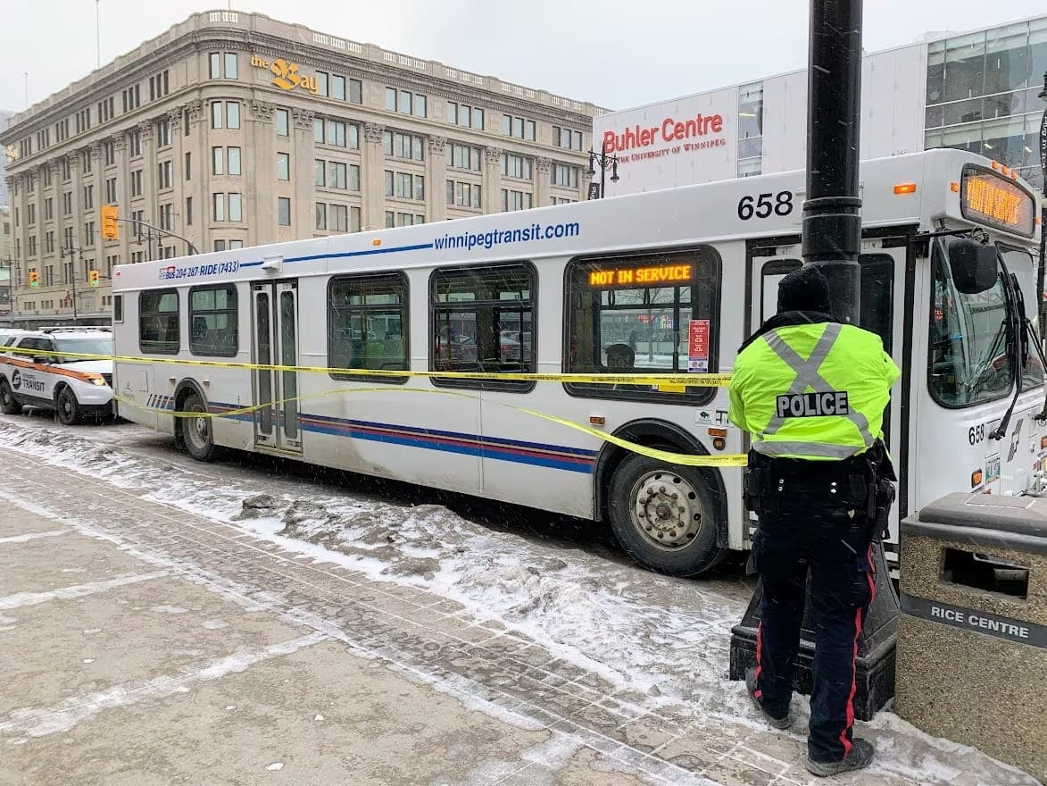 A police officer stands next to a Winnipeg Transit bus that has been roped off with caution tape.