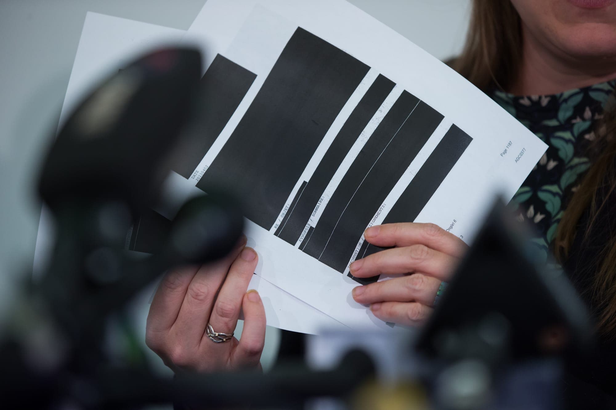 A woman holds pages of paper that have been significantly redacted.