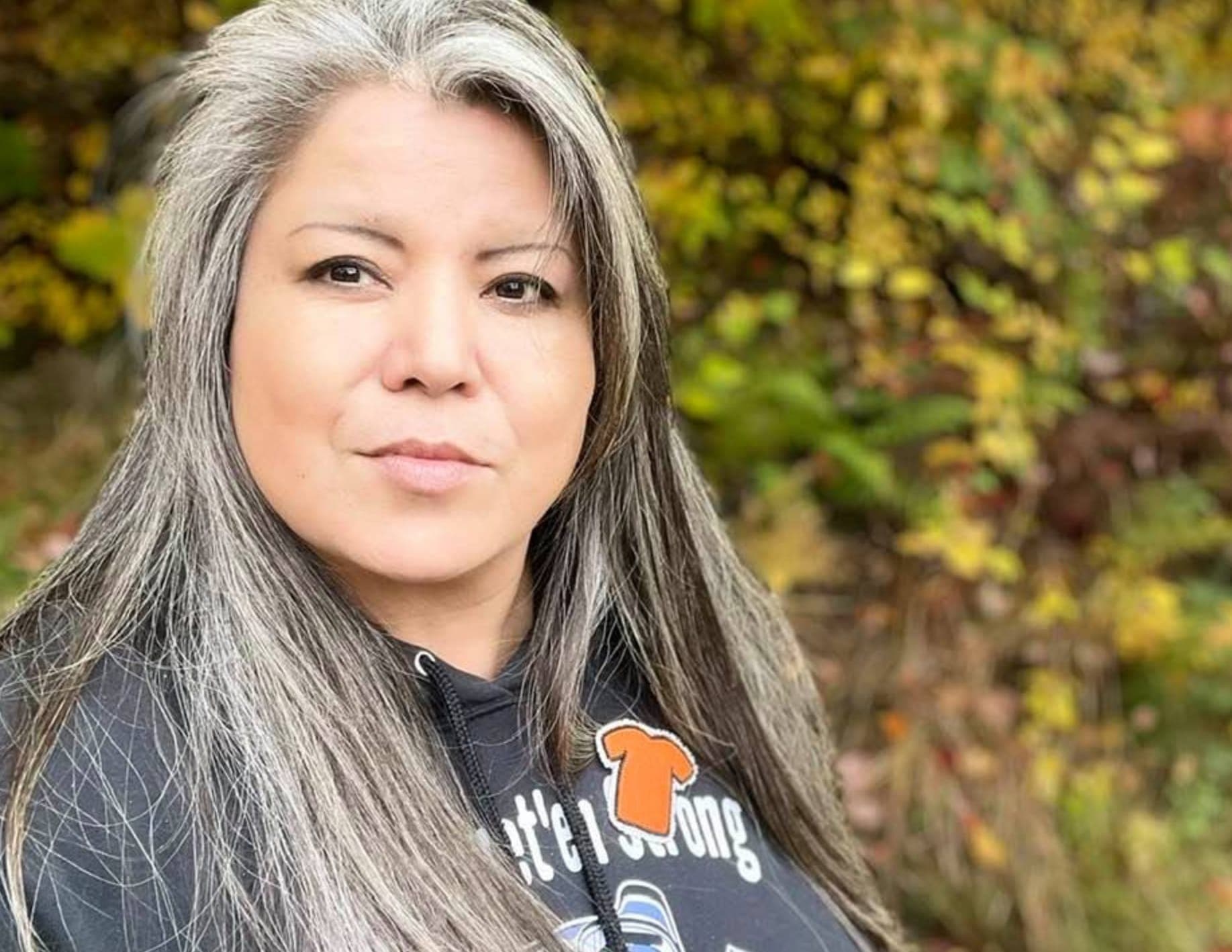 A woman with grey and black hair poses outdoors in a sweatshirt.