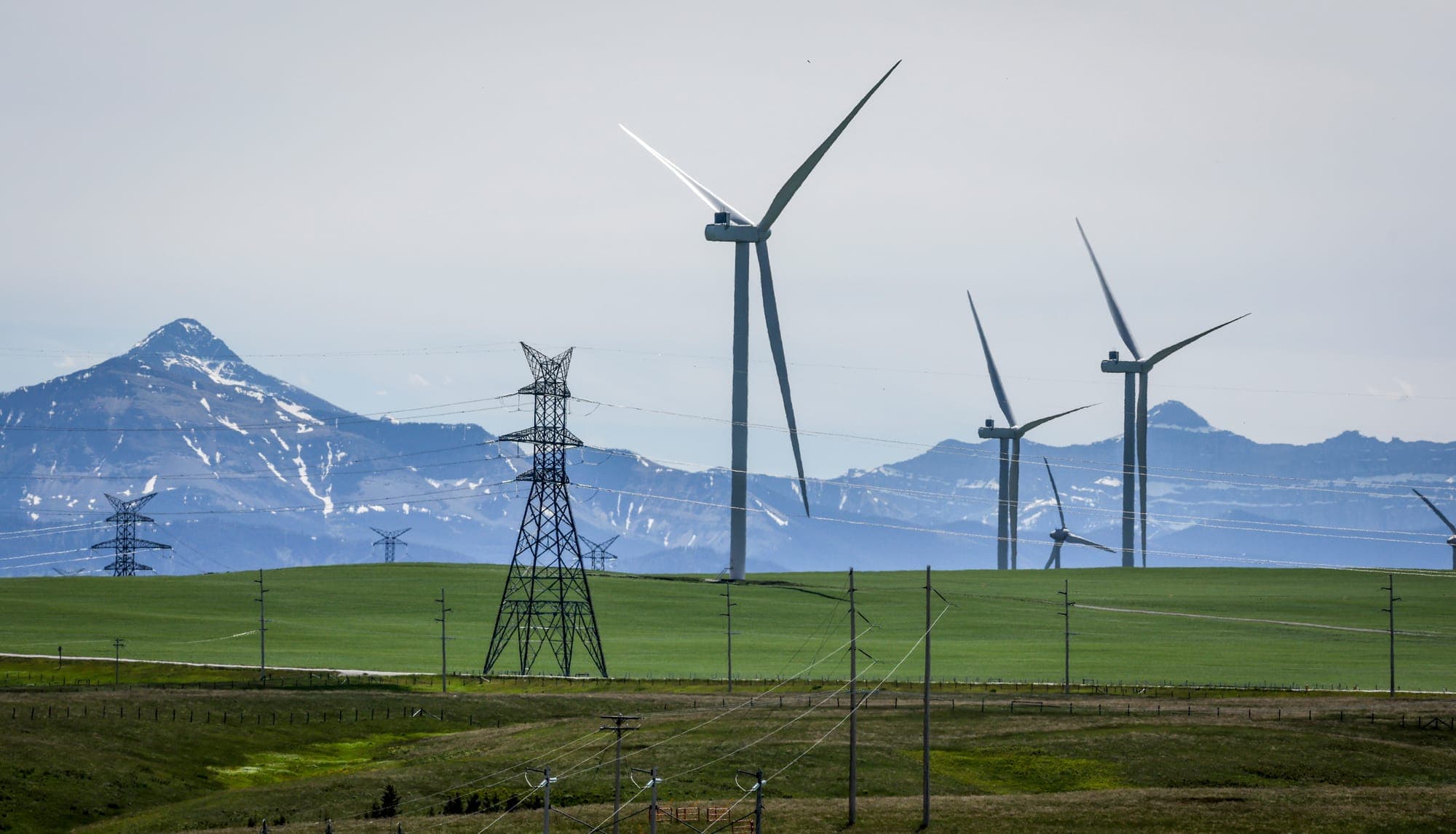 Power transmission lines and wind turbines as seen with the Rocky Mountains in the background near Pincher Creek, Alta., on June 6, 2024.