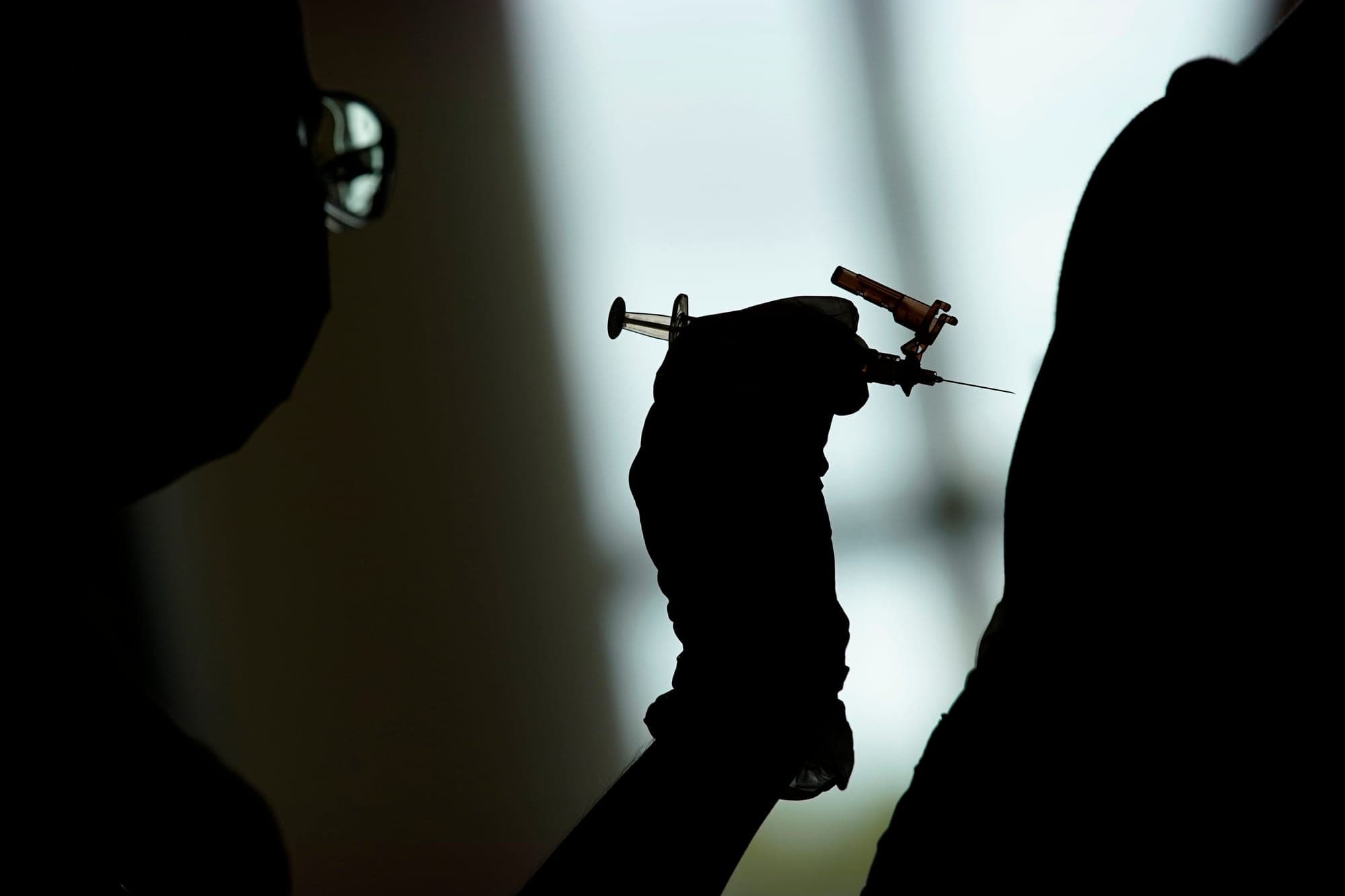 A health professional is shown in silhouette administering a vaccine.