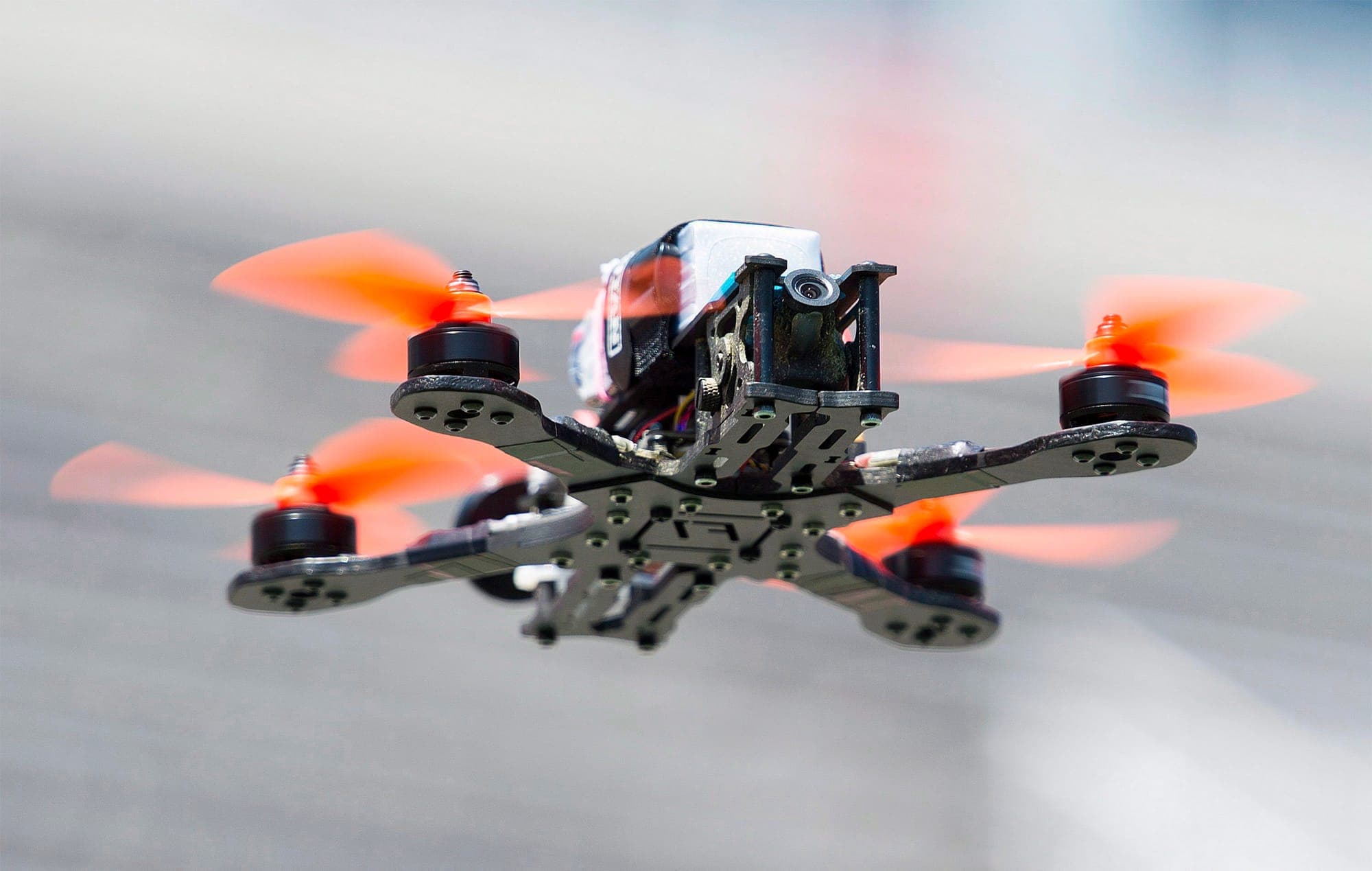 A drone with four orange copter wings hovers in the air.