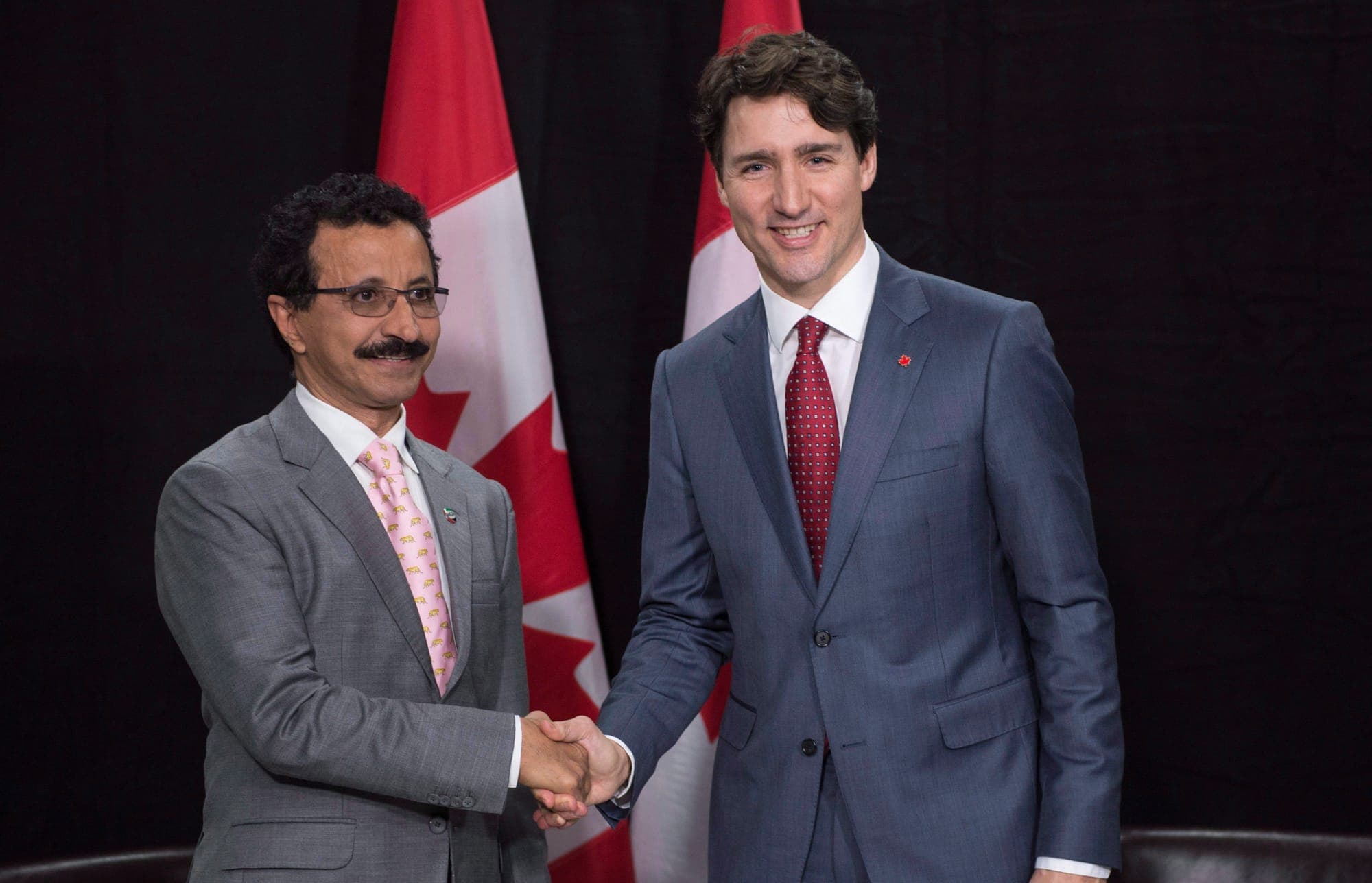 Sultan Ahmed bin Sulayem and Justin Trudeau smile and shake hands in front of two Canadian flags.