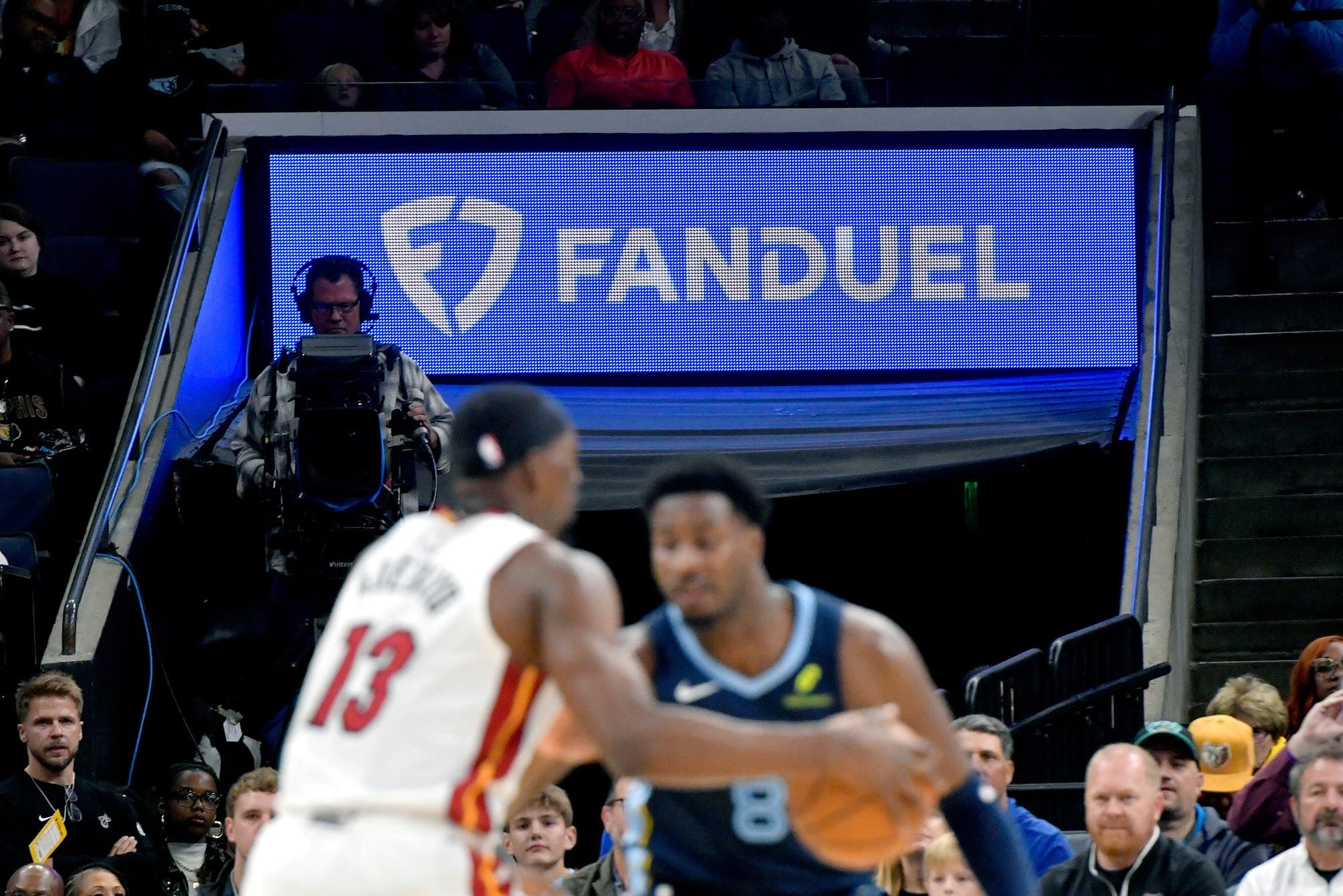 Two basketball players are in the foreground with a digital FanDuel sign behind them.