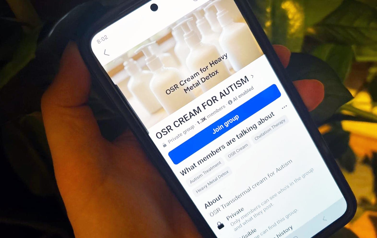 A hand holds a phone displaying a Facebook page titled OSR CREAM FOR AUTISM.
