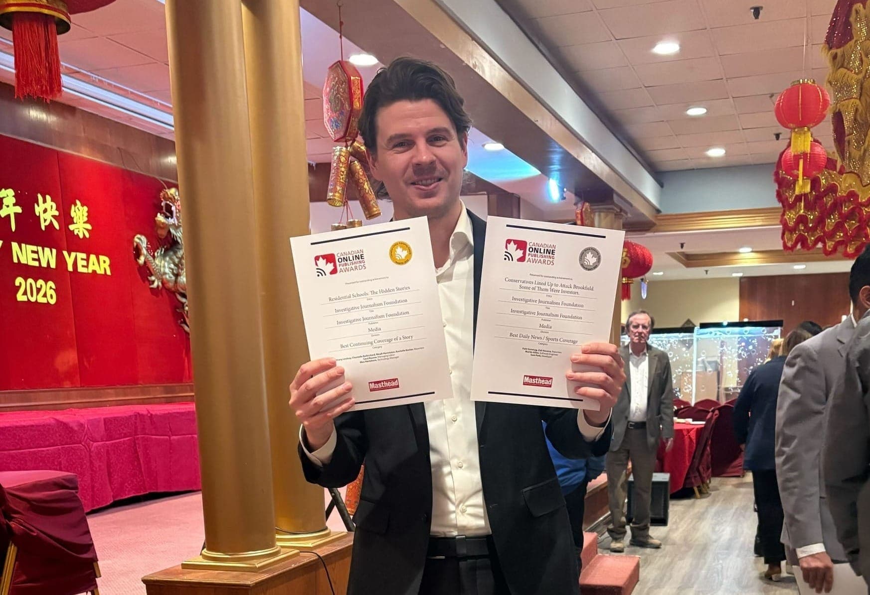 IJF technology manager Max Hartshorn holds two sheets of paper representing online publishing awards in a Chinese restaurant.
