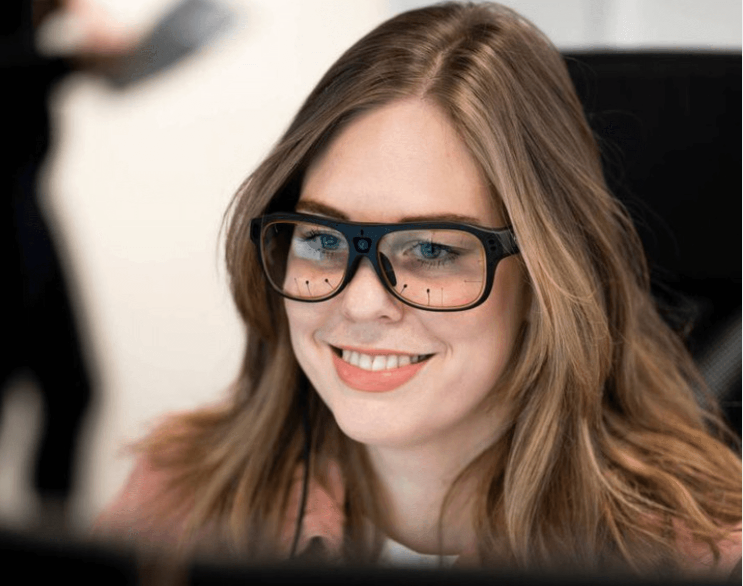 A woman wears thick-framed Tobii eye-tracking glasses.
