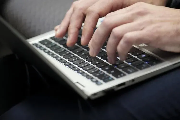 Fingers are shown typing on a laptop.