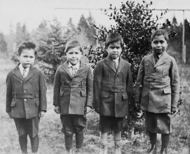 A black and white image of four young boys standing in the yard of the Alberni Residential School.