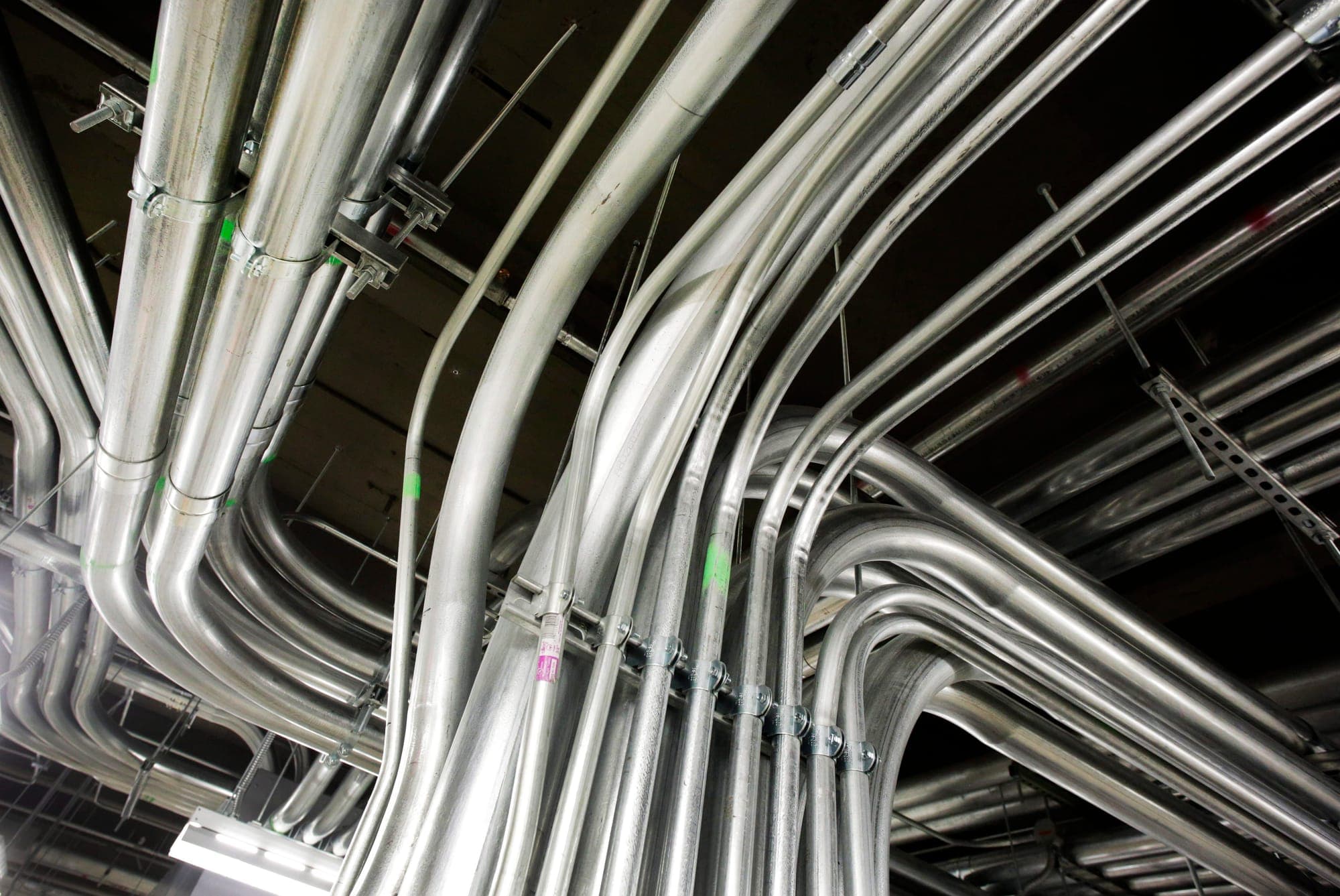 A maze of silver electrical pipes hang from a ceiling.