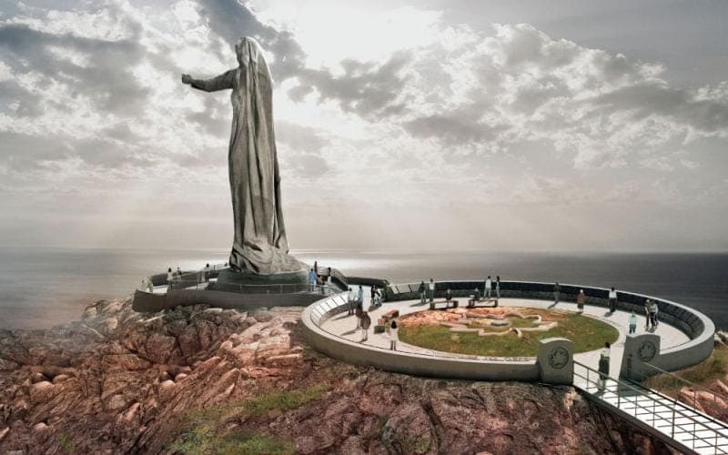 A white statue of a woman with her arms outstretched to the sea.